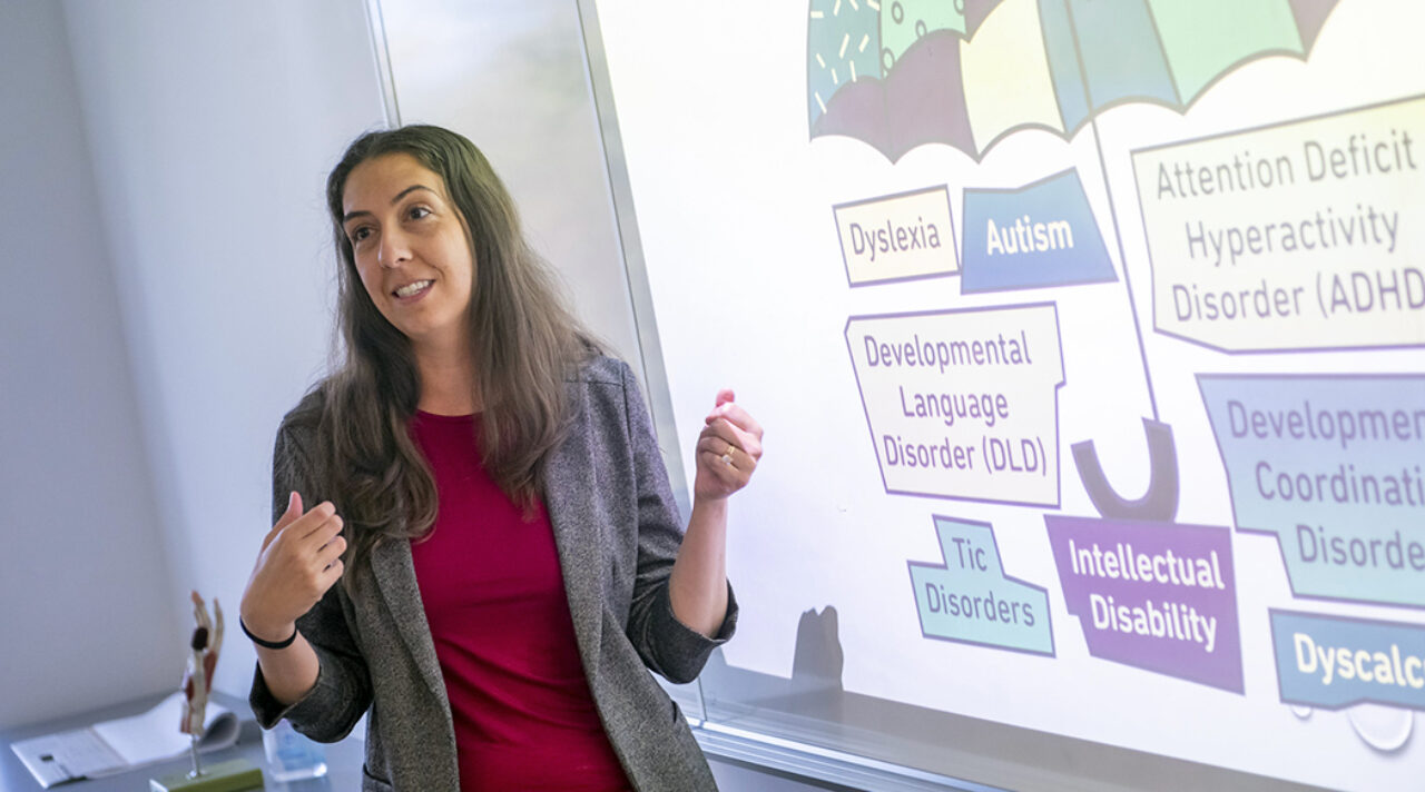 Woman gestures at a projector screen and teaches.