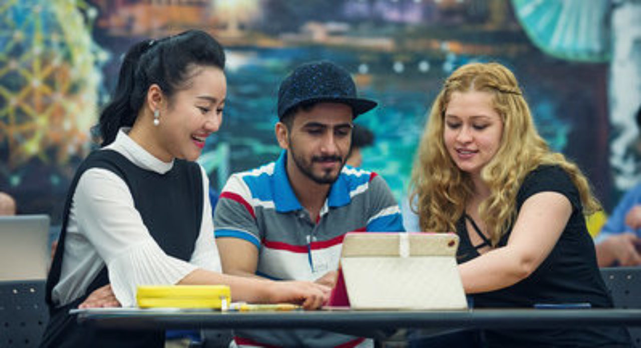 three students outside gathered around a computer tablet