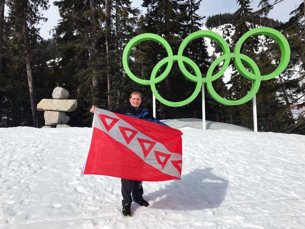 Orsini holding the flag of his fraternity, Tau Kappa Epsilon, in front of the Olympic Rings on Cypress Mountain in British Columbia, Canada.