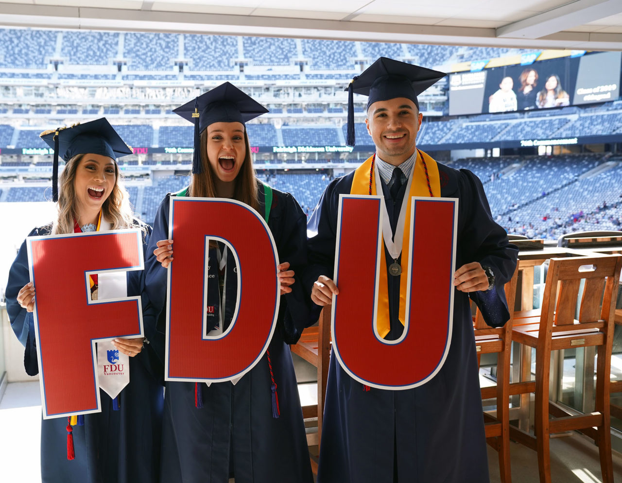 three graduates holding FDU sign