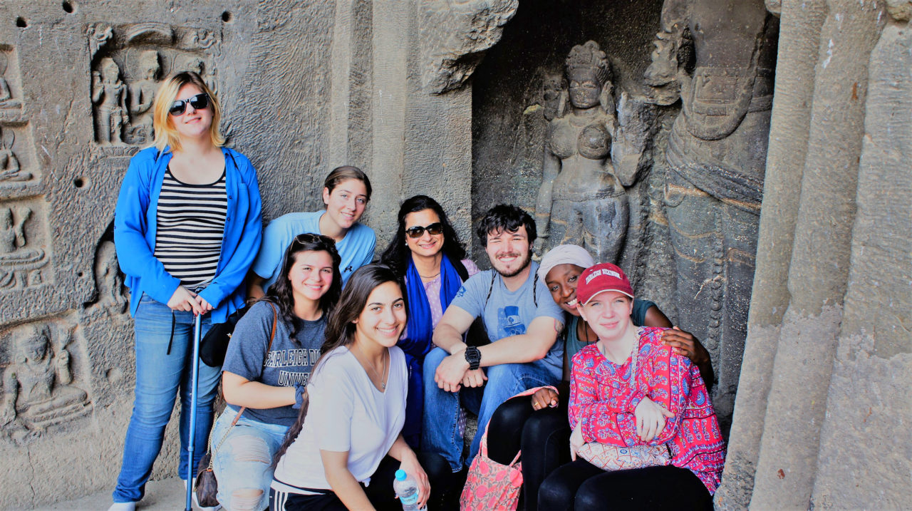 Students and Professor Kiron Sharma (center with blue scarf) gather around with caves as the backdrop.