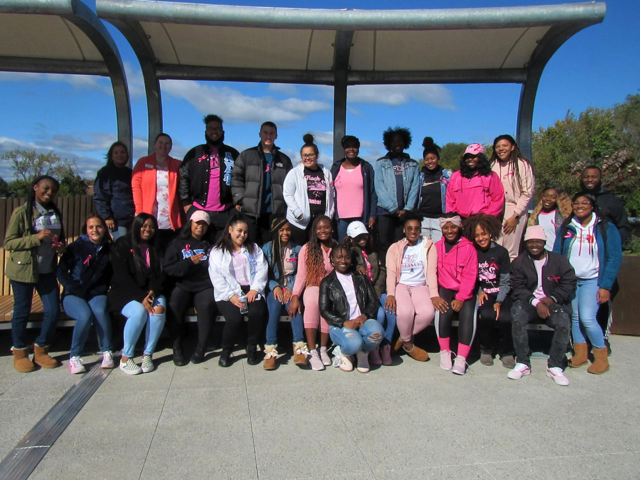 A group of students in pink clothes pose for a photo on the Metro Campus footbridge.