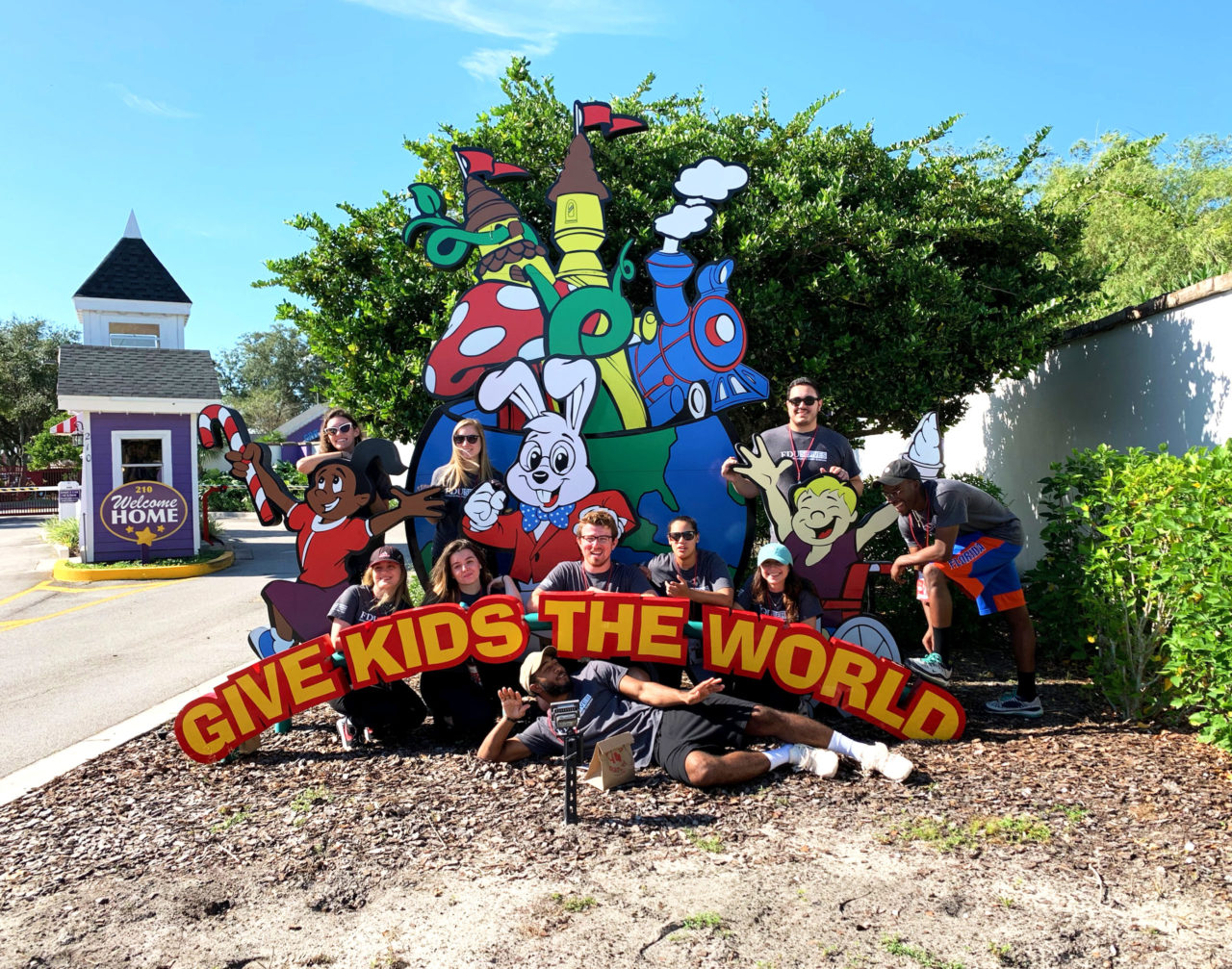 A group of students pose in front of a sign that reads "Gives Kids the World."