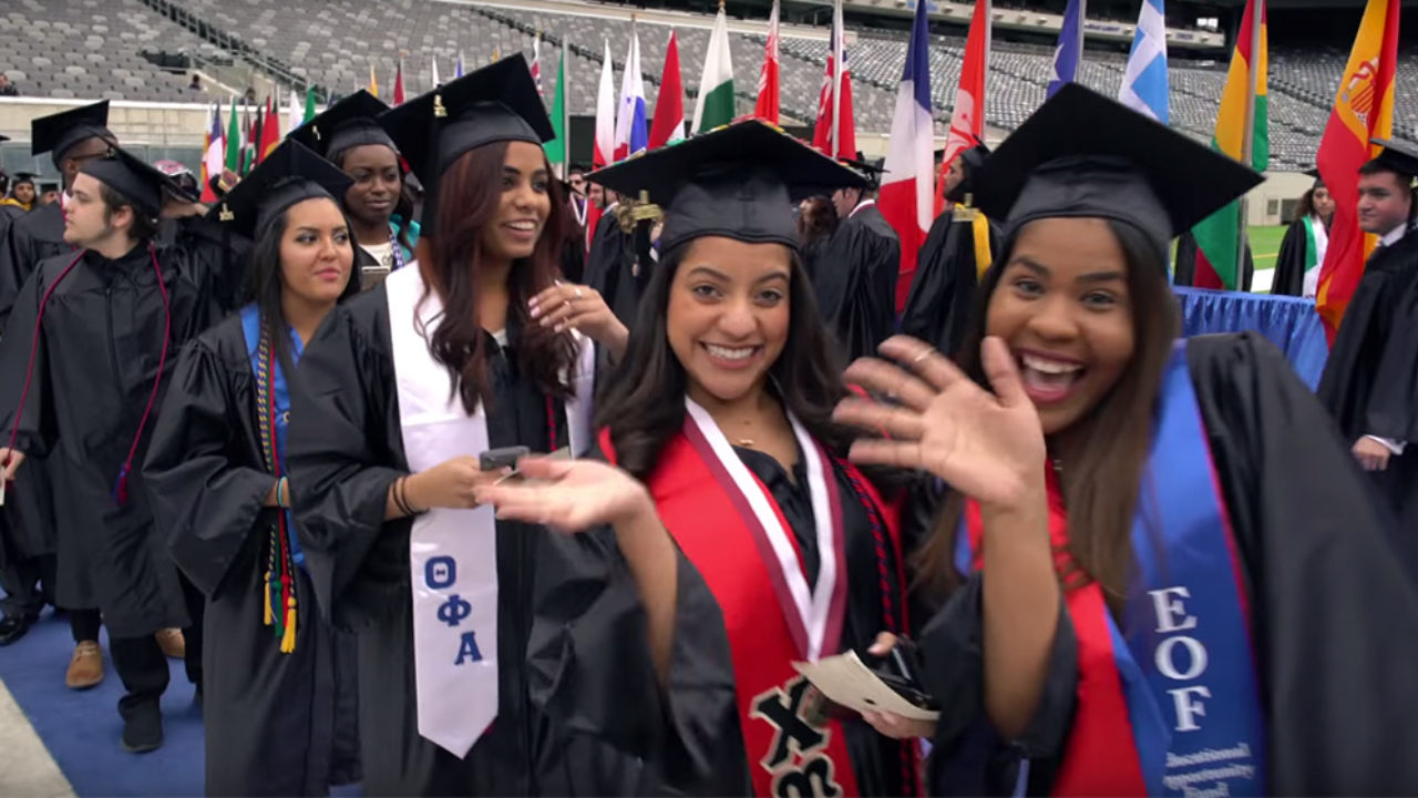 Students smile at wave in cap and gowns at graduation
