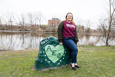 Student sits near a rock painted with Greek Life letters.