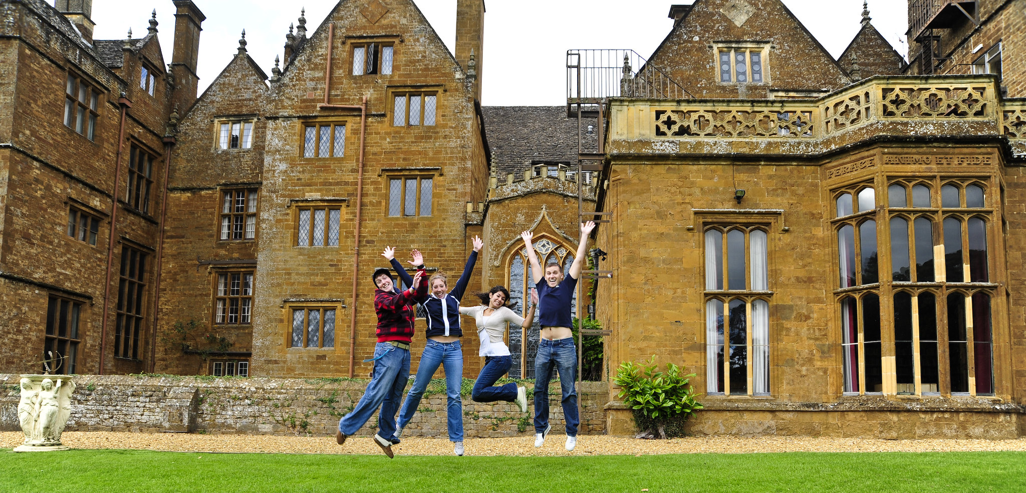 Wroxton Abbey in the background, with students jumping joy in the foreground.