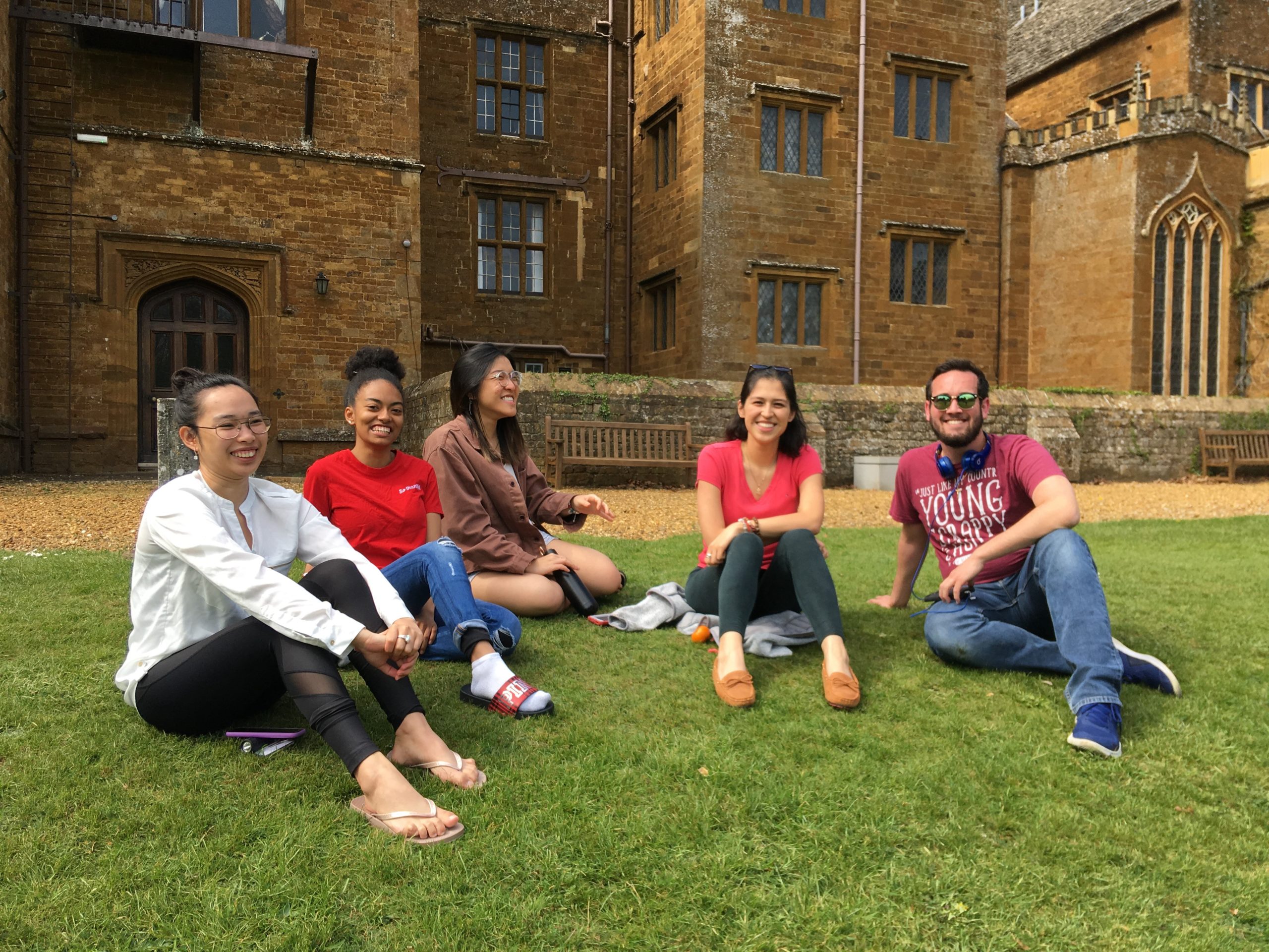 Students sit and smile in front of the Wroxton Abbey