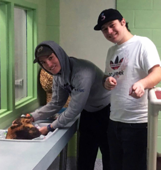 One student pets a cat while the other smiles and points at the camera