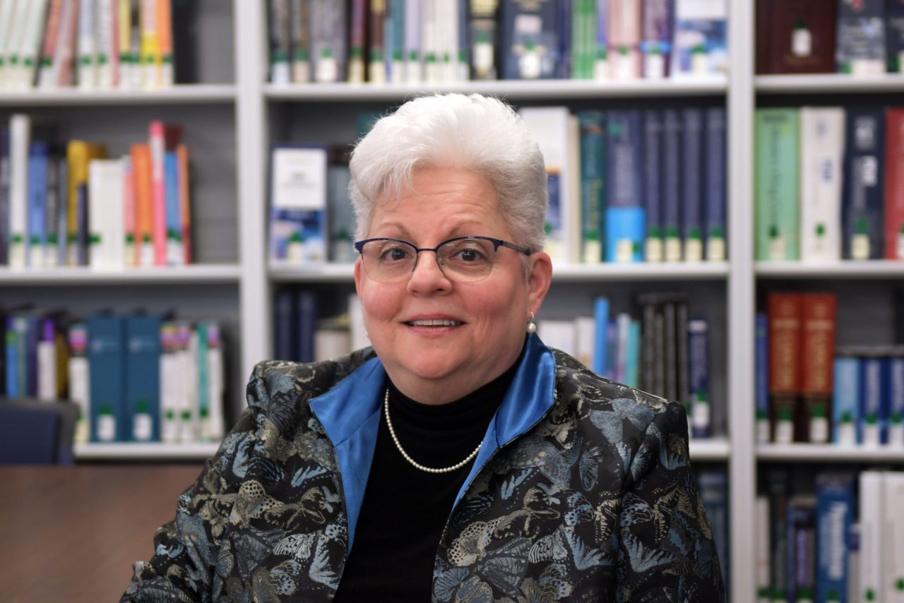 Middle-aged woman sits in front of a bookshelf and smiles.