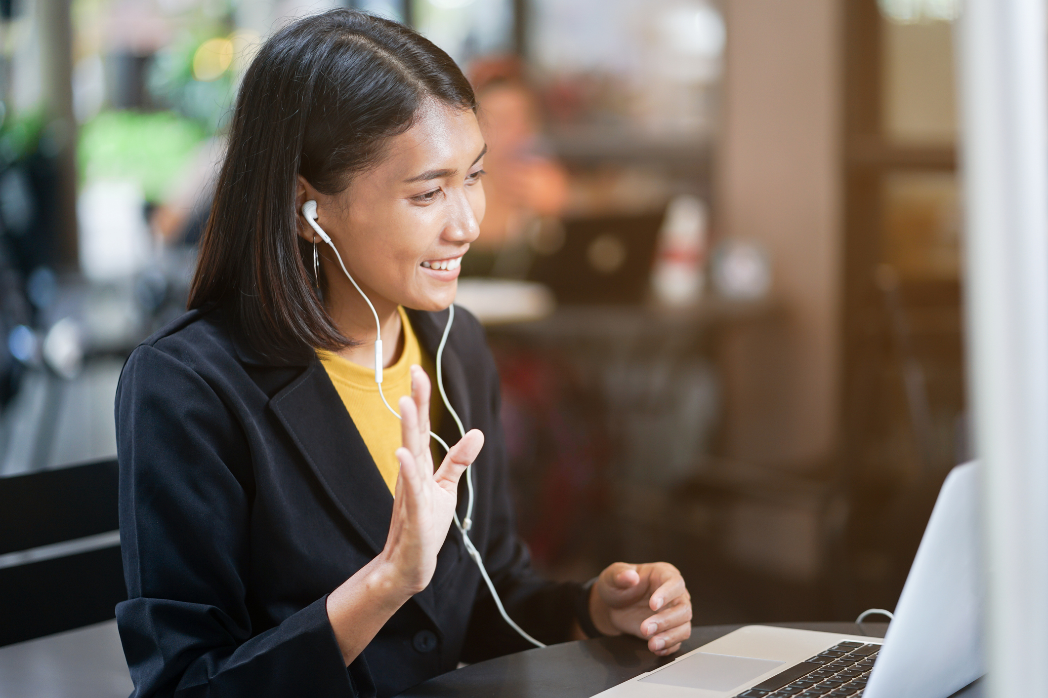 A woman with headphones on waves at someone she is video chatting with on a laptop