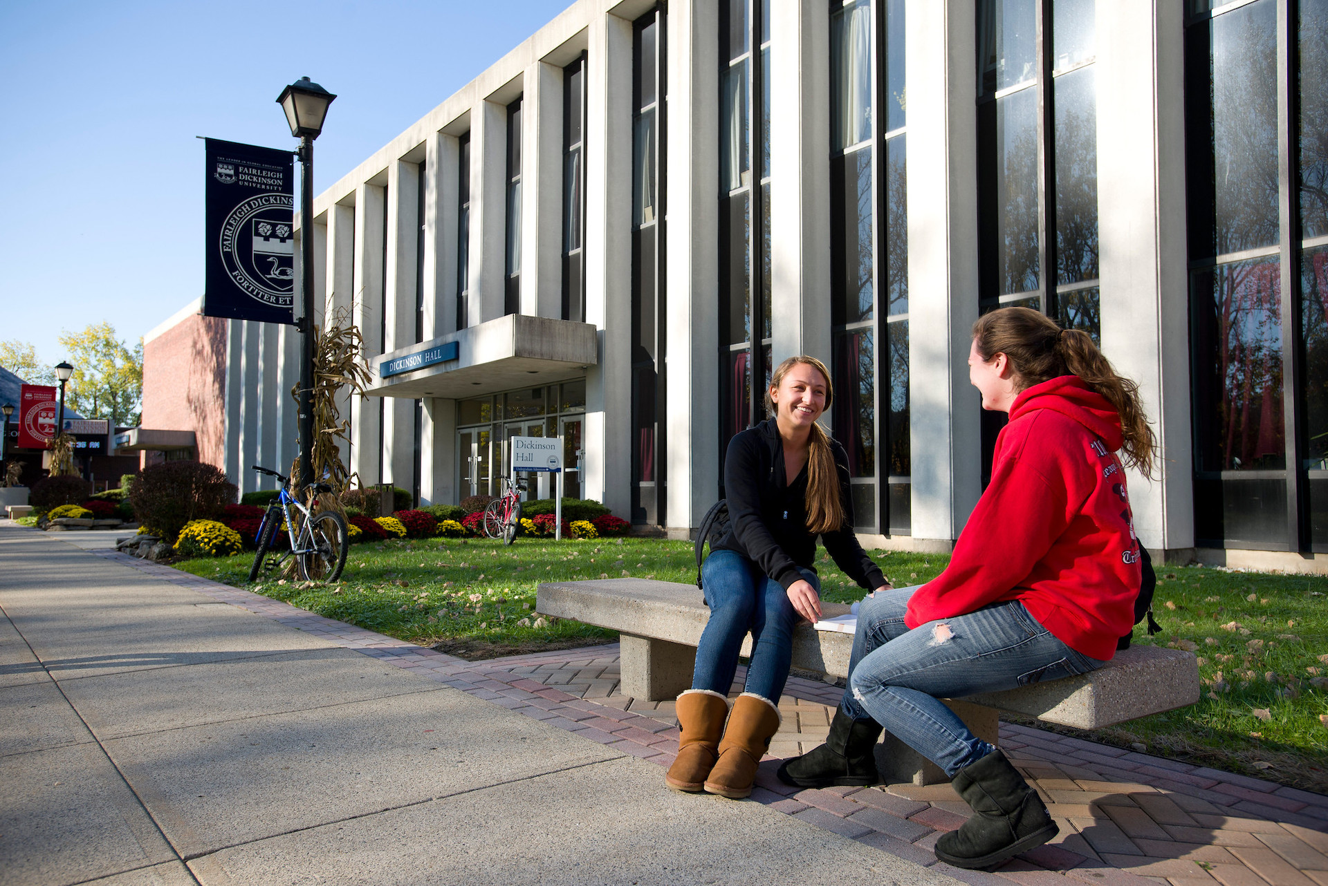 Two girls sit on a bench in front of a building.