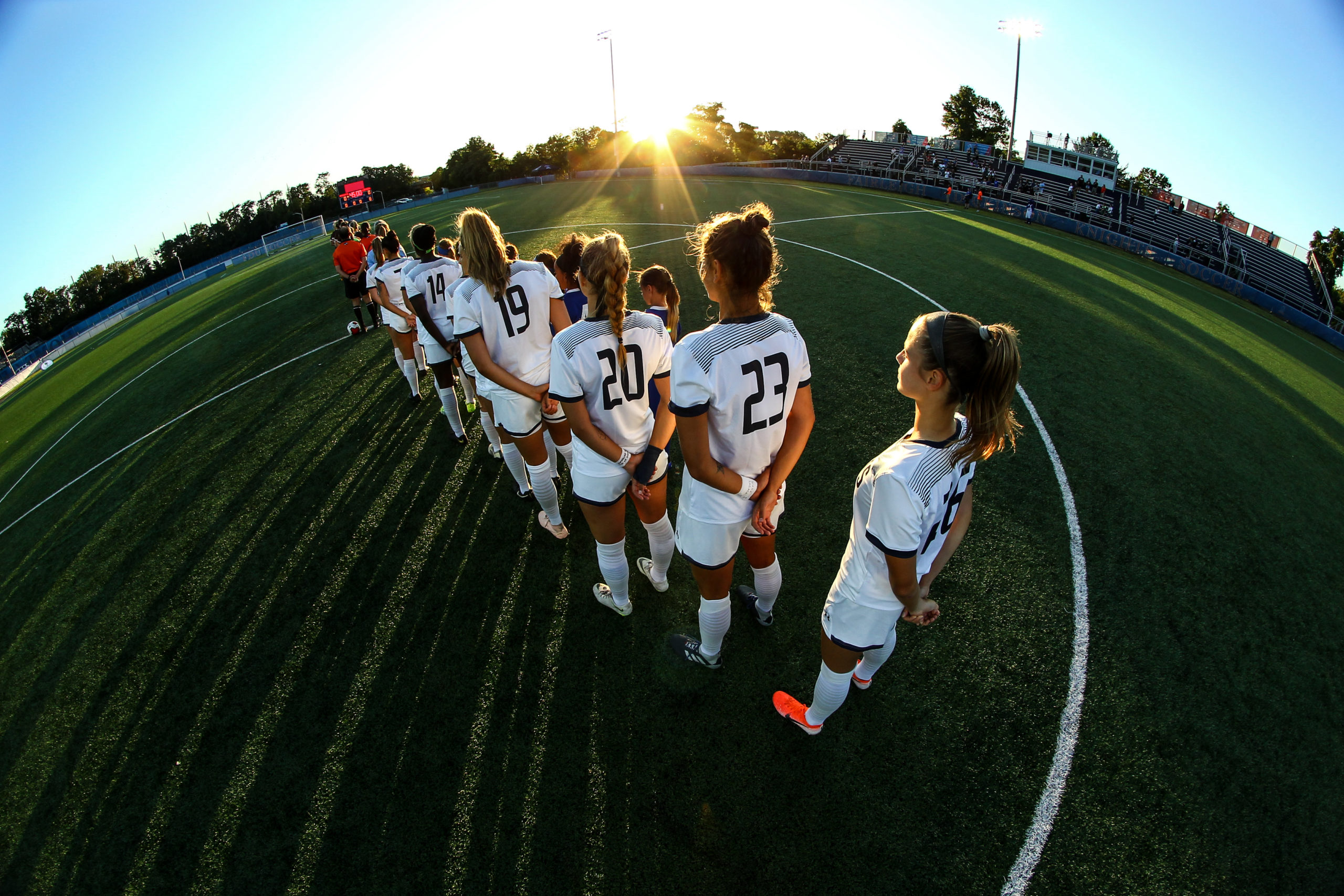 Seven soccer players stand in a line on a soccer field.