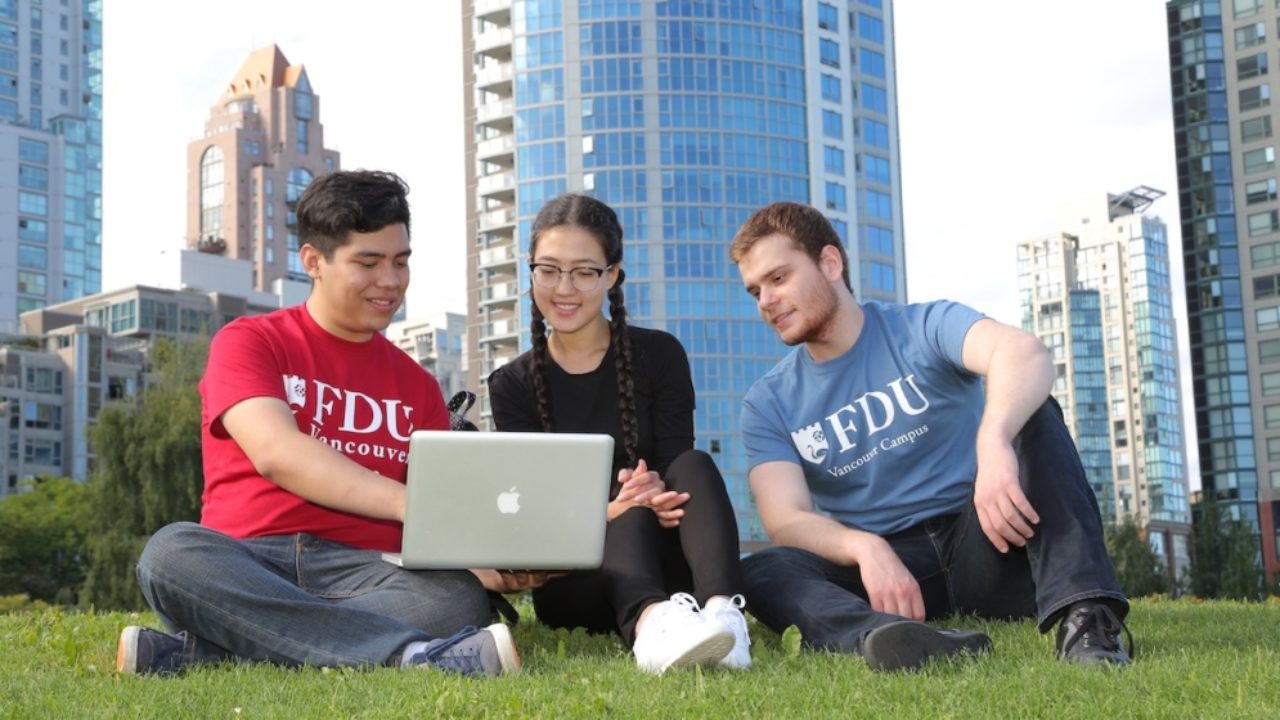 Three students sitting on the lawn looking at a laptop