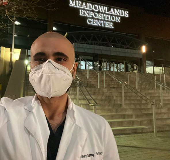 A male pharmacist wearing a mask stands outside of a temporary hospital built at the Meadowlands Exposition Center.