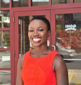 A young woman stands outside of an IHOP restaurant.