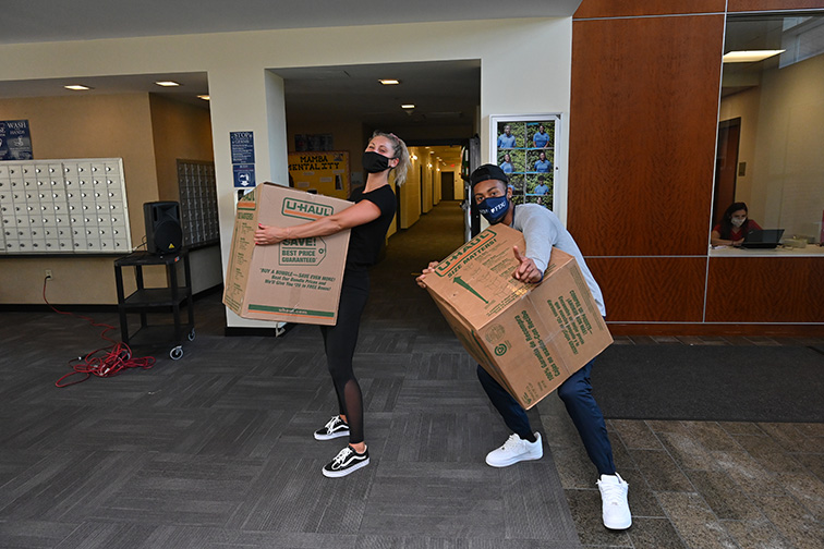 Two students haul huge boxes into a residence hall on move-in day.