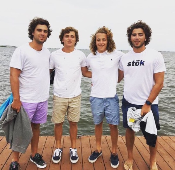 Four young men pose on a dock by the water. 