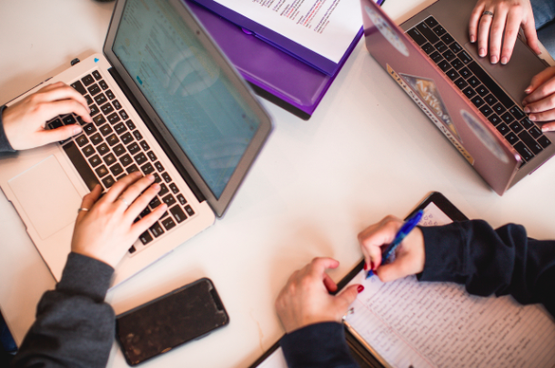 Close up photo of laptops, a smartphone and study materials on a table.