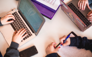 Close up photo of laptops, a smartphone and study materials on a table.