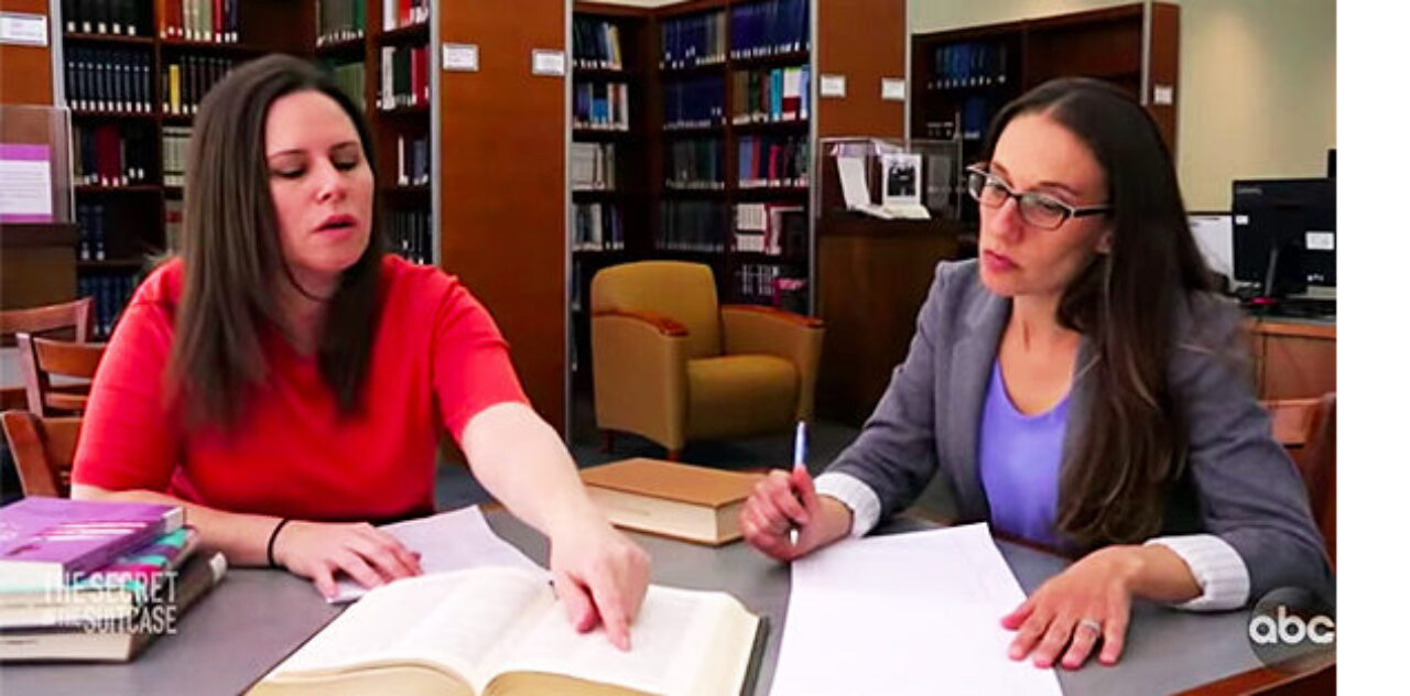 Two female professors review notes at a table in the library.