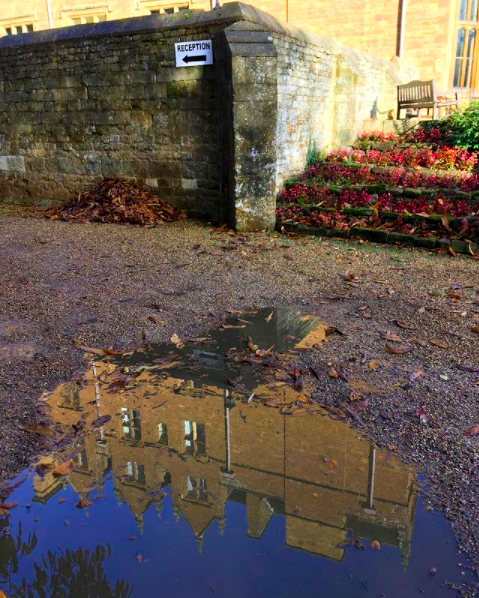 A puddle clearly reflects an image of Wroxton Abbey.