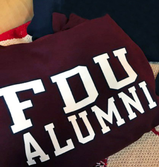 A pile of FDU-branded alumni gear, including a sweatshirt and a hat.