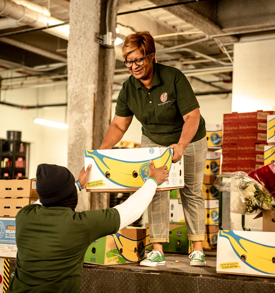 A woman hands another person a crate of food donations.