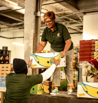 A woman hands another person a crate of food donations.