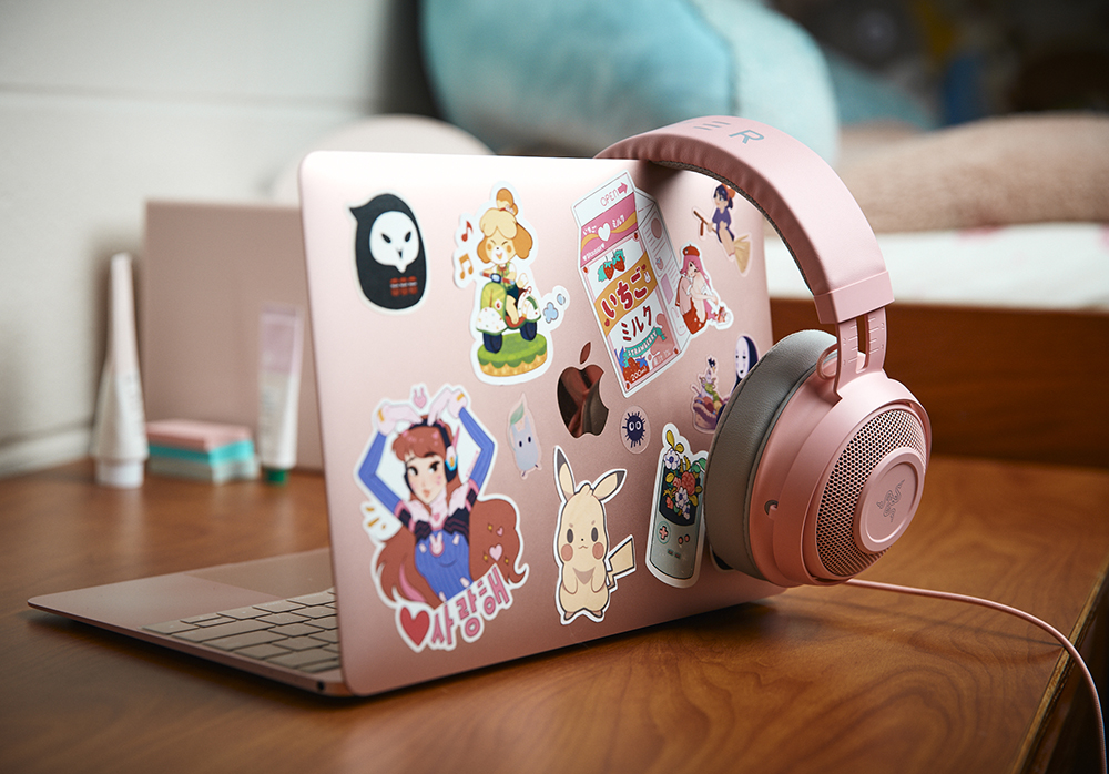 A pink laptop computer, with pink headphones draped over the side, features lots of stickers.