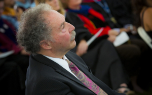 A man in a suit sits in a crowd at convocation.