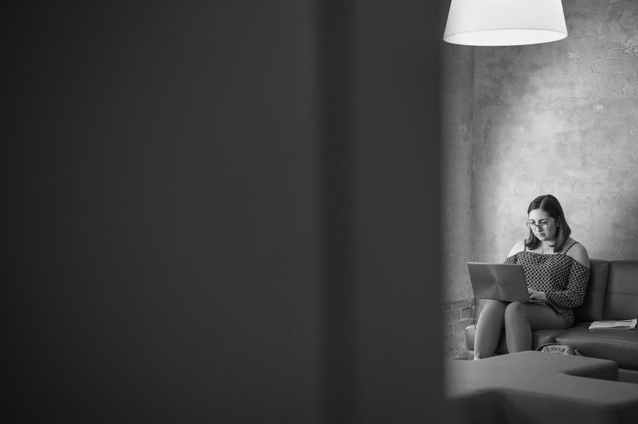 A person sits on a couch on a laptop. Photo is taken from behind a doorframe.