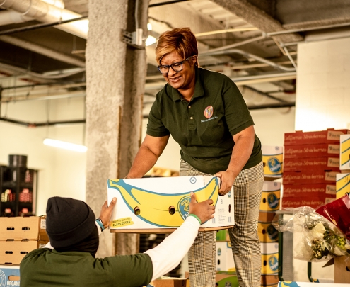 A woman hands another person a crate of food donations.