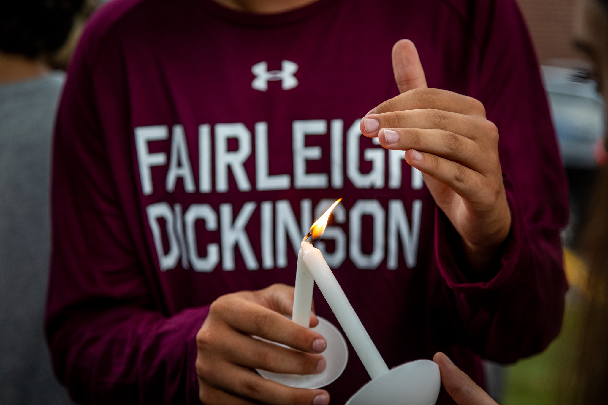 A close up photo of a student wearing an FDU sweatshirt, lighting a candle at a welcome ceremony.