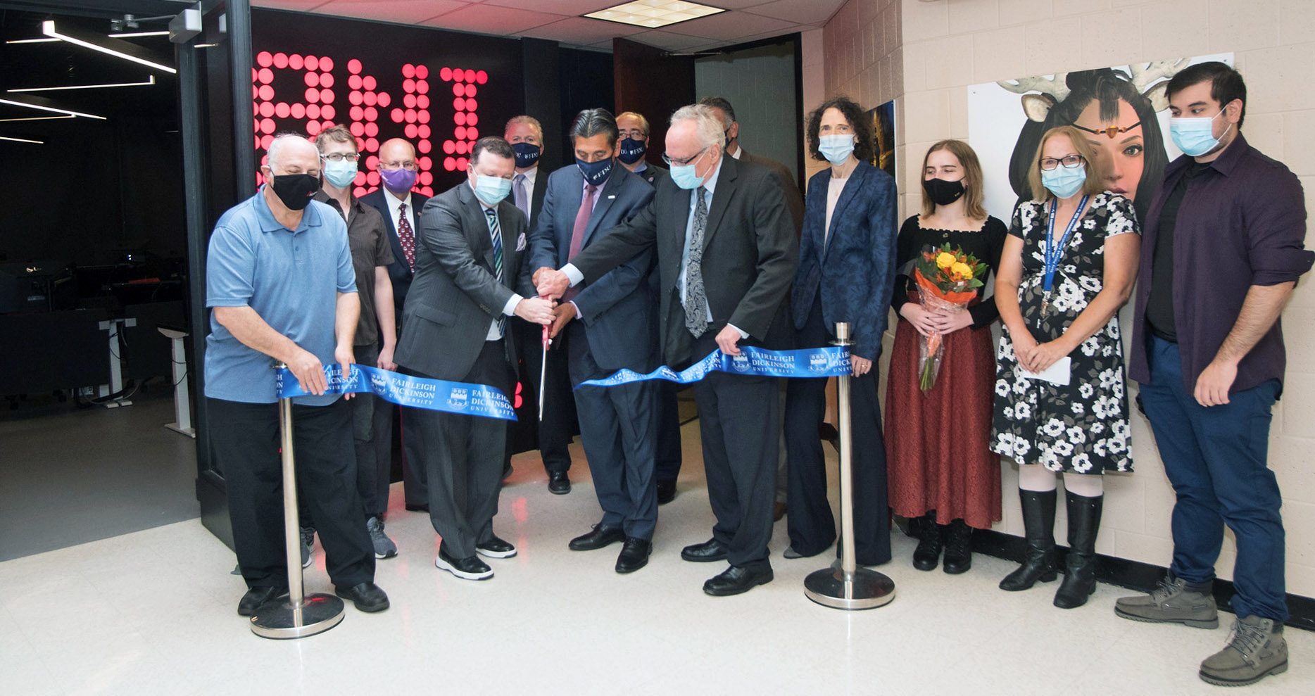 A group of people stand in a row to cut a celebratory ribbon.