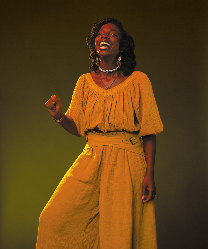 Portrait of a woman wearing a jumpsuit, in mid-laugh.