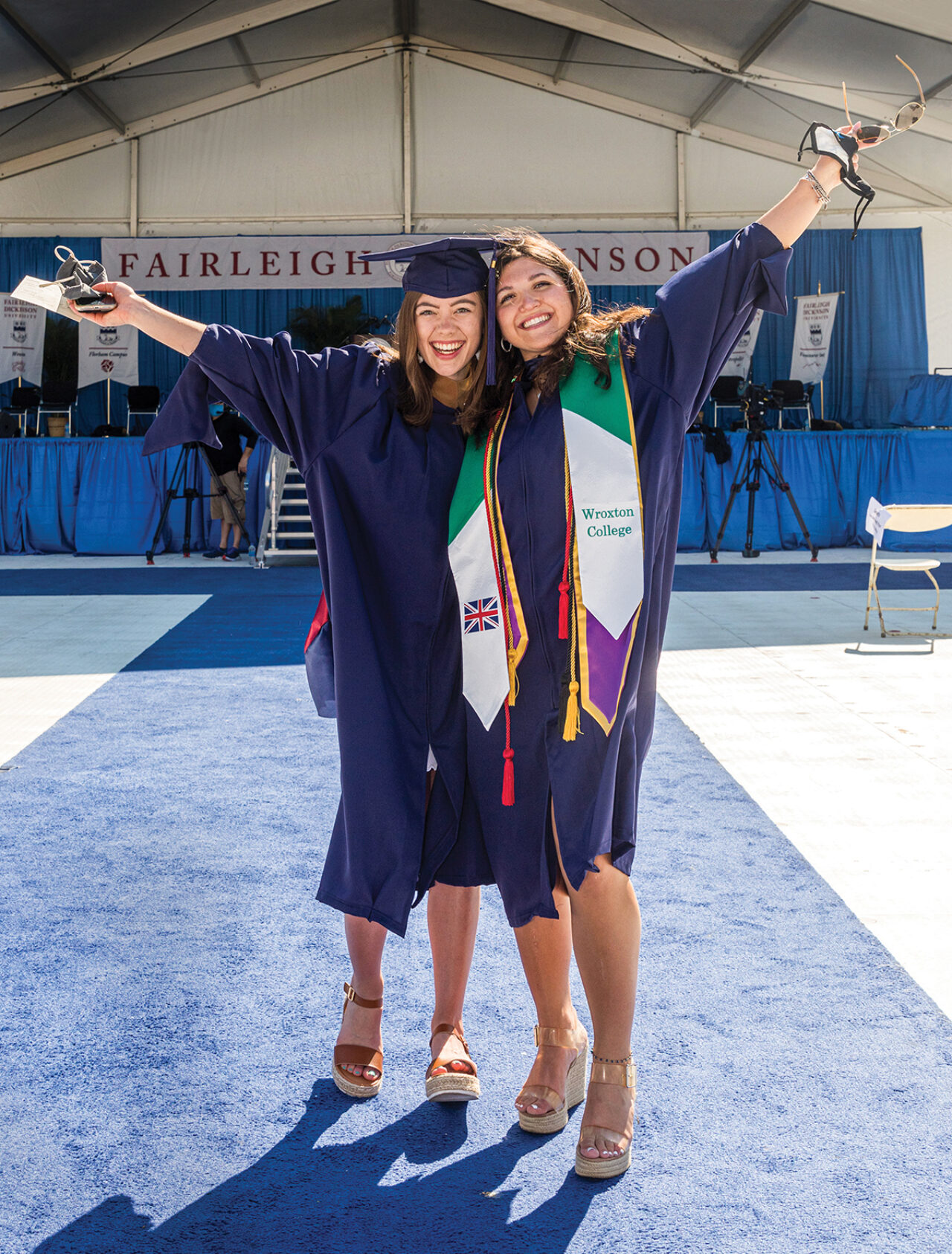 Two young female graduates fling their arms out wide.