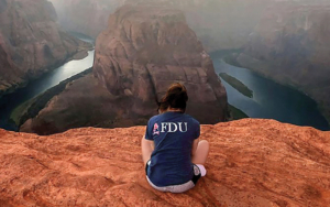 A young woman wearing an FDU shirt looks out over Horseshoe Bend.