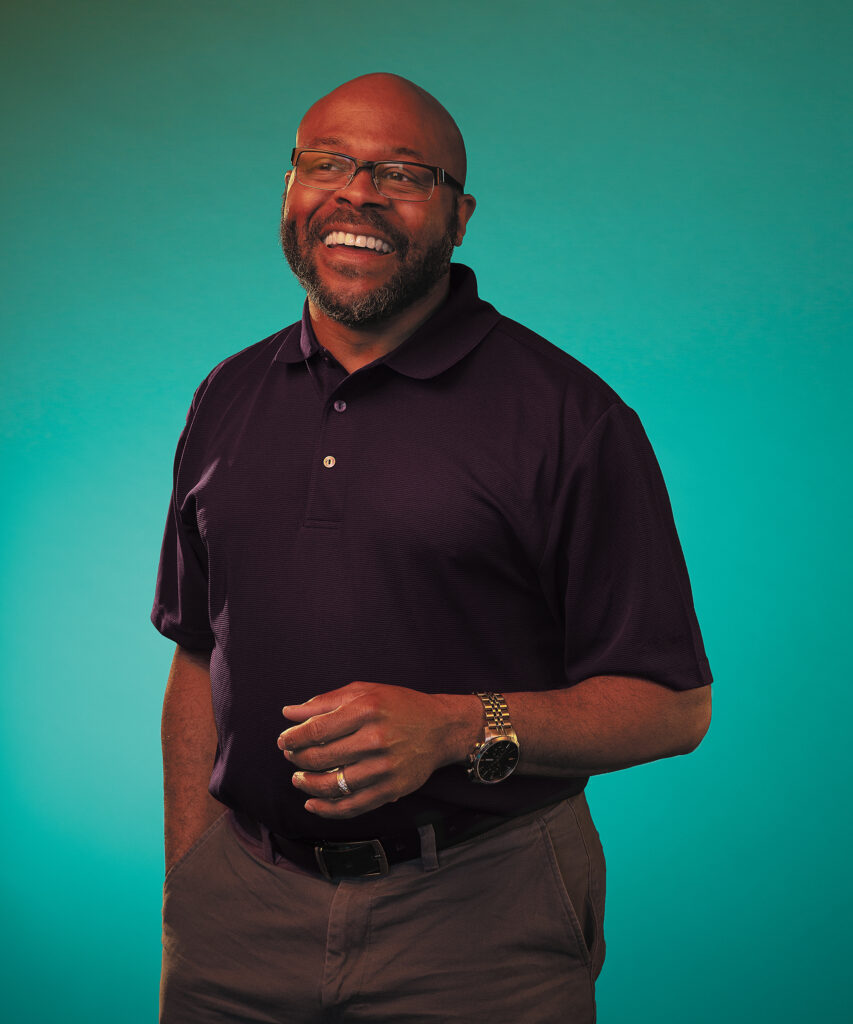 A man wearing glasses smiles broadly in a portrait photo.