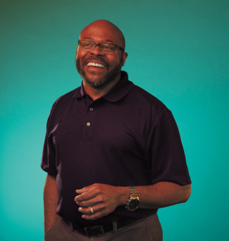 A man wearing glasses smiles broadly in a portrait photo.