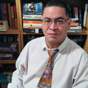 Portrait of a male faculty member wearing a tie. There are bookcases behind him.