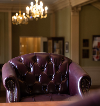 An empty leather chair with chandeliers hanging above in a hallway.