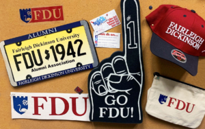 A foam finger, an FDU baseball hat, a magnet, a FDU sticker and more pinned to a corkboard.