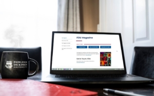 An FDU coffee mug, books and an open laptop on a table.