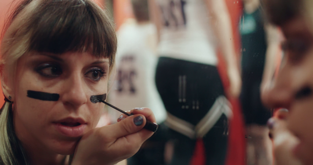 A roller derby girl applies make up in a mirror.