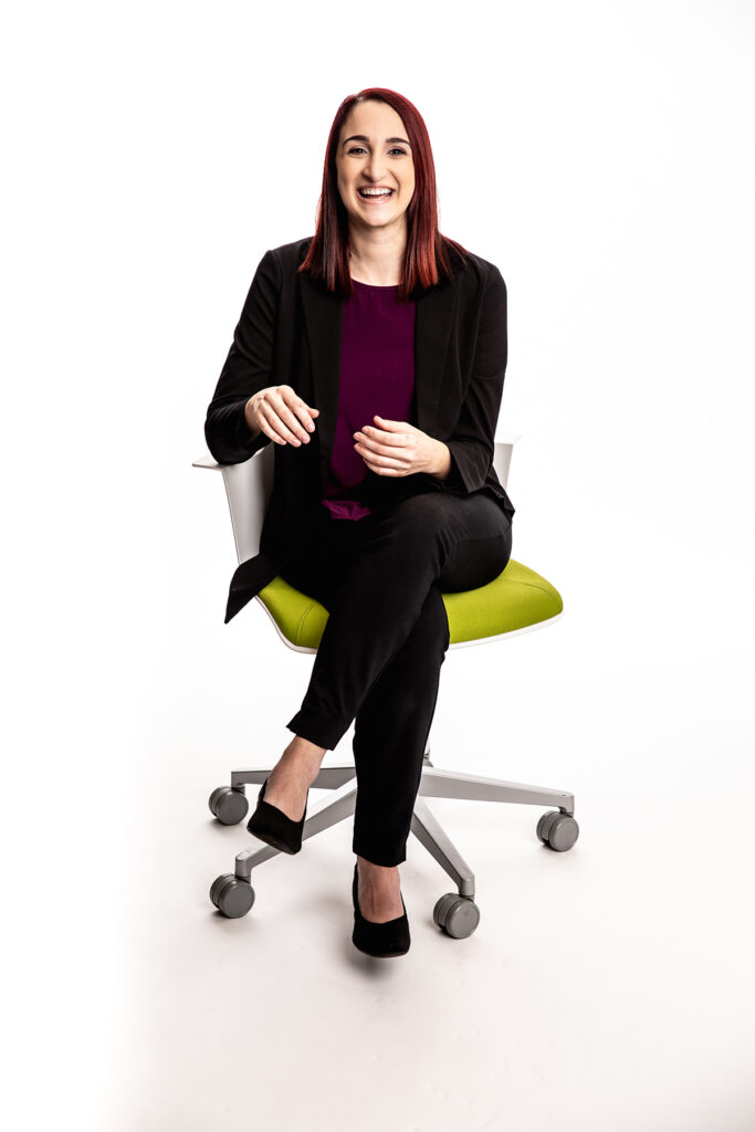 Portrait of a woman sitting on a desk chair and smiling.