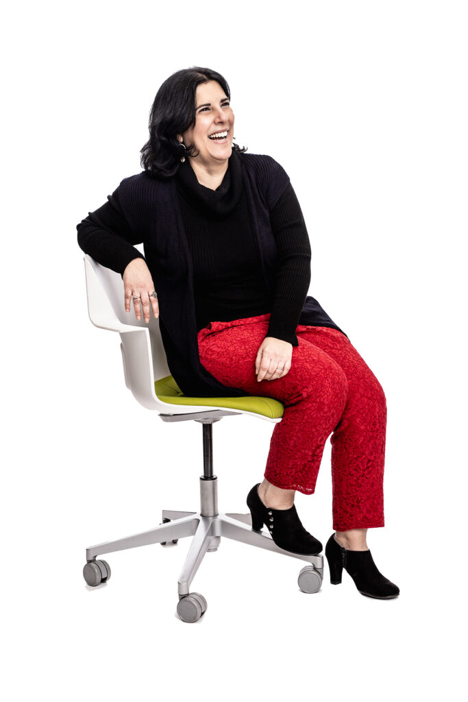 Portrait of a woman sitting in a desk chair, with an open and inviting stance.