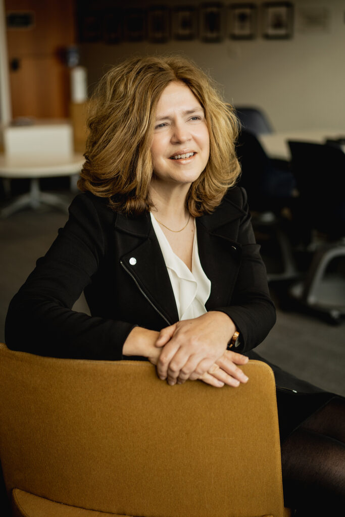 Portrait of a woman sitting in a desk chair, smiling into the distance.