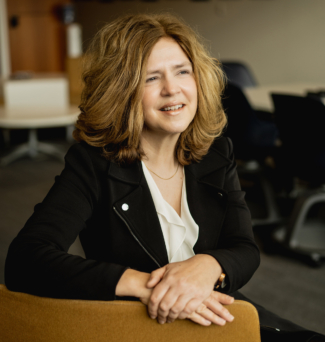 Portrait of a woman sitting in a desk chair, smiling into the distance.