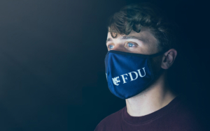 A young man wears a face mask, branded for FDU.