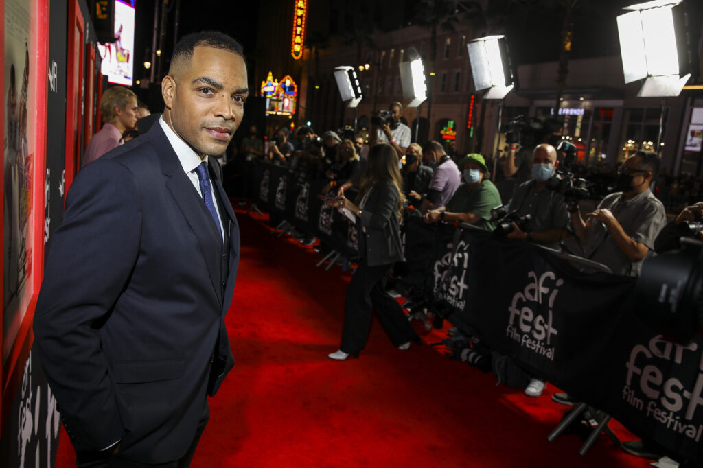 A man in a suit walks the red carpet at a movie premiere.